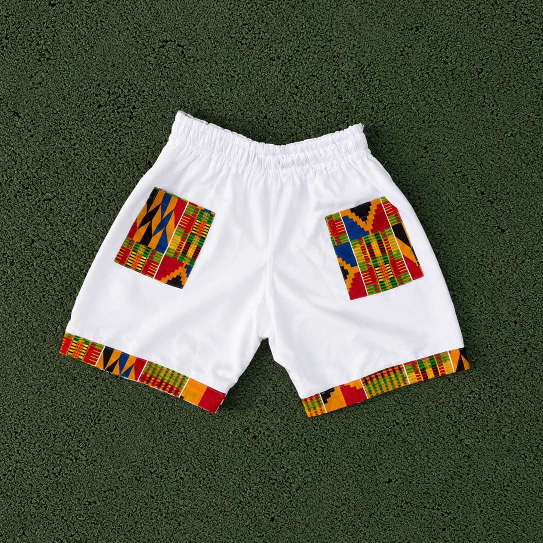 White athletic shorts with colorful African Kente pattern trim on the leg openings, laid flat on a dark green textured background.